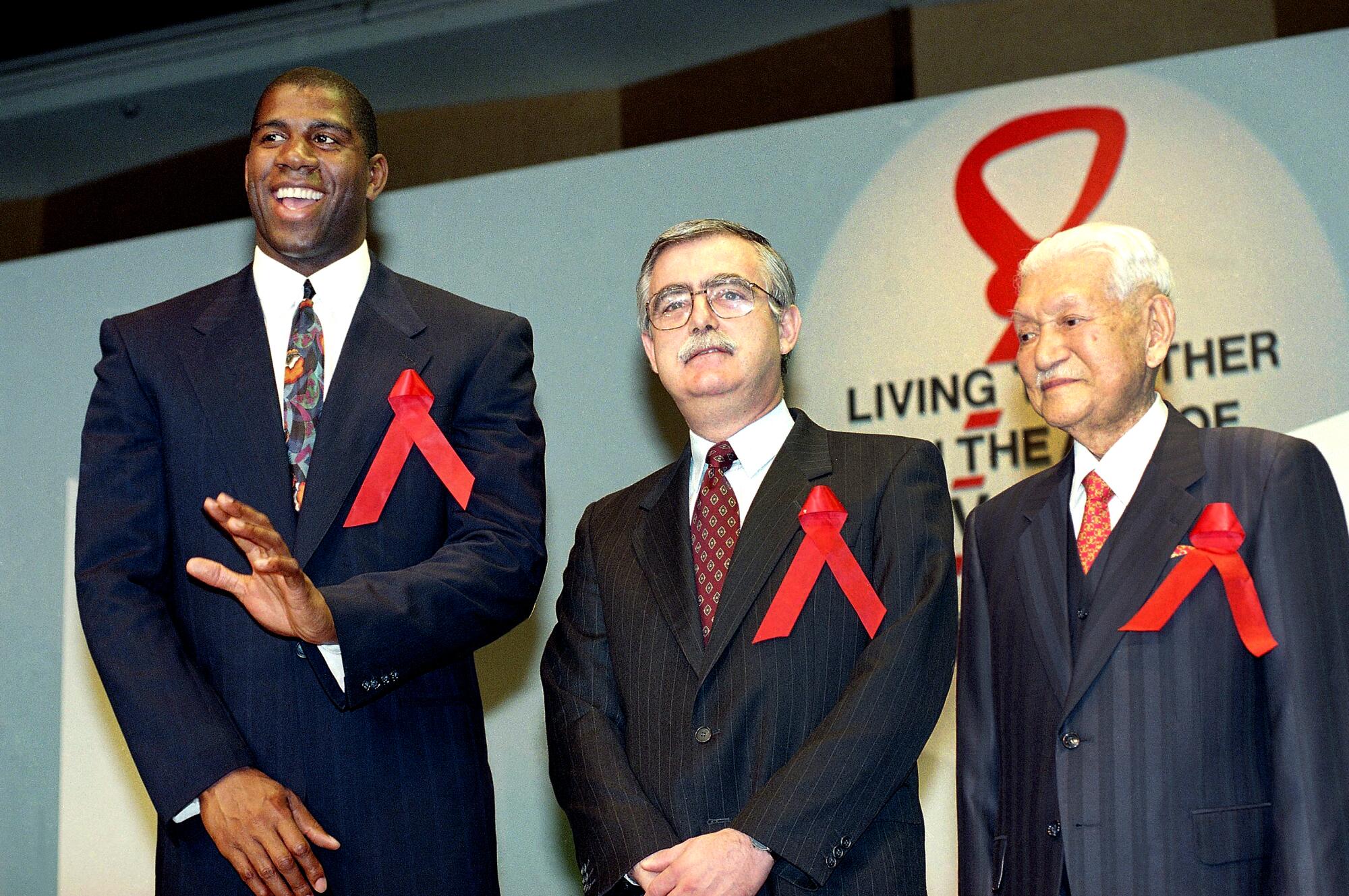 Magic Johnson, Michael Merson and Ryoichi Sasagawa wear oversize red ribbons on their suit jackets