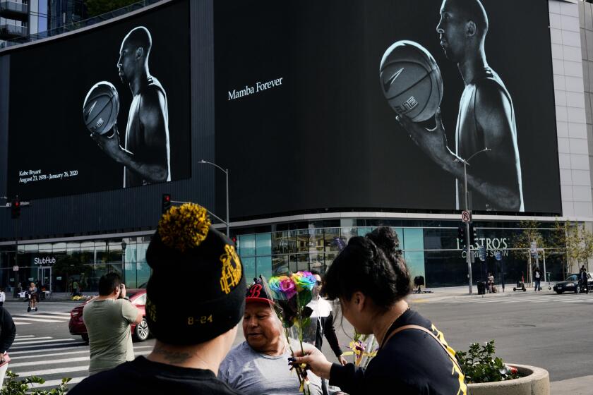 A vendor sells flowers to Kobe Bryant fans in front of a giant electronic billboard featuring the NBA star near the Staples Center in downtown Los Angeles on Thursday, Jan. 30, 2020. People wearing Kobe Bryant jerseys, hats, shoes and other gear continued to arrive by the thousands at the downtown arena where Bryant had made basketball history. (AP Photo/Richard Vogel)