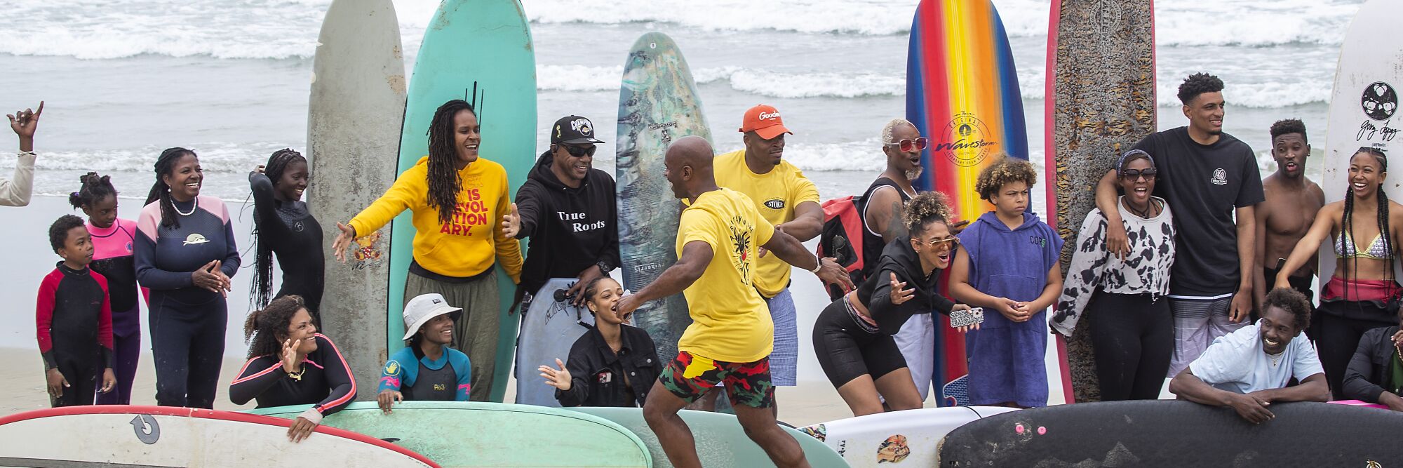 Nathan Fluellen high-fives surfers posing for group photos near the Huntington Beach pier.
