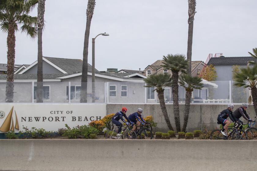 NEWPORT BEACH, CALIF. -- TUESDAY, MARCH 31, 2020: People ride bikes past the Newport Beach welcome sign amid Coronavirus social distancing regulations in Newport Beach, Calif., on March 31, 2020. (Allen J. Schaben / Los Angeles Times)