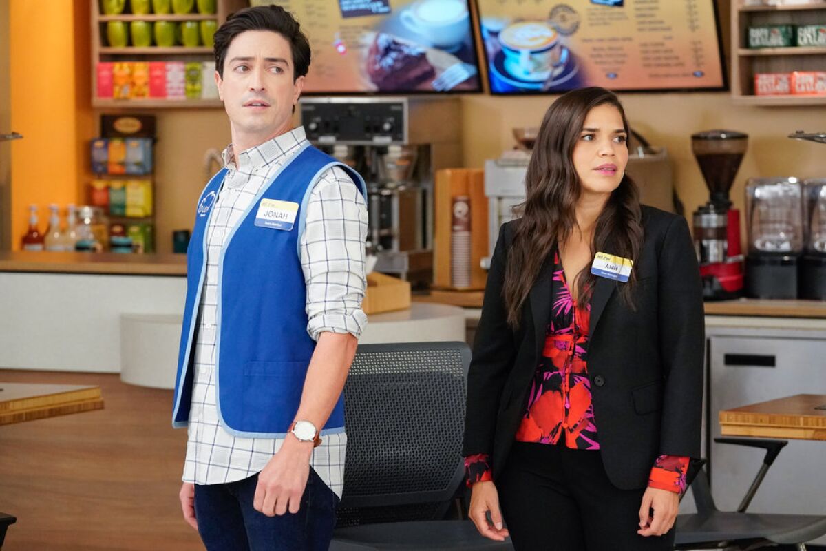 Jonah (Feldman) and Amy (Ferrera) stand in their work outfits in front of a coffee bar.