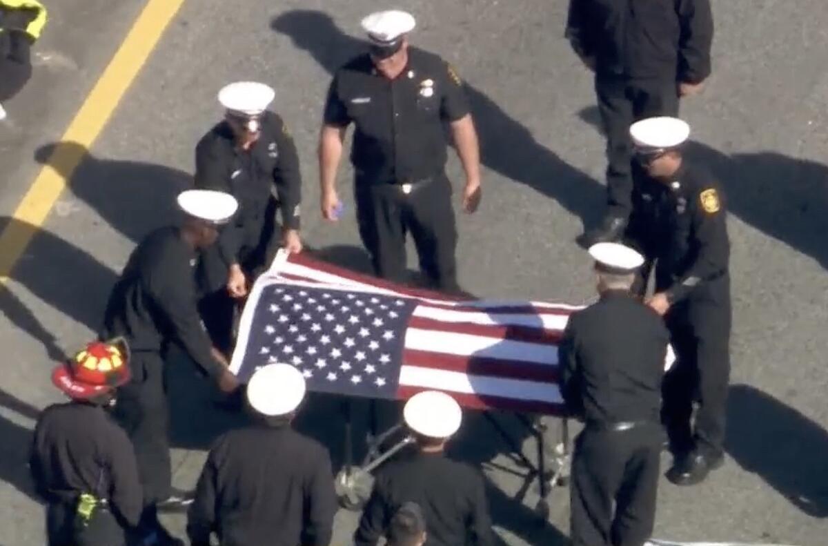An aerial view of firefighters in white hats and dress uniform placing an American flag over a casket as others stand by
