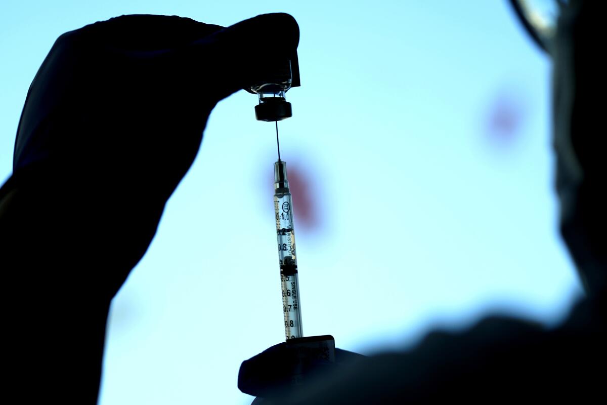 A healthcare worker fills a syringe from a vial.