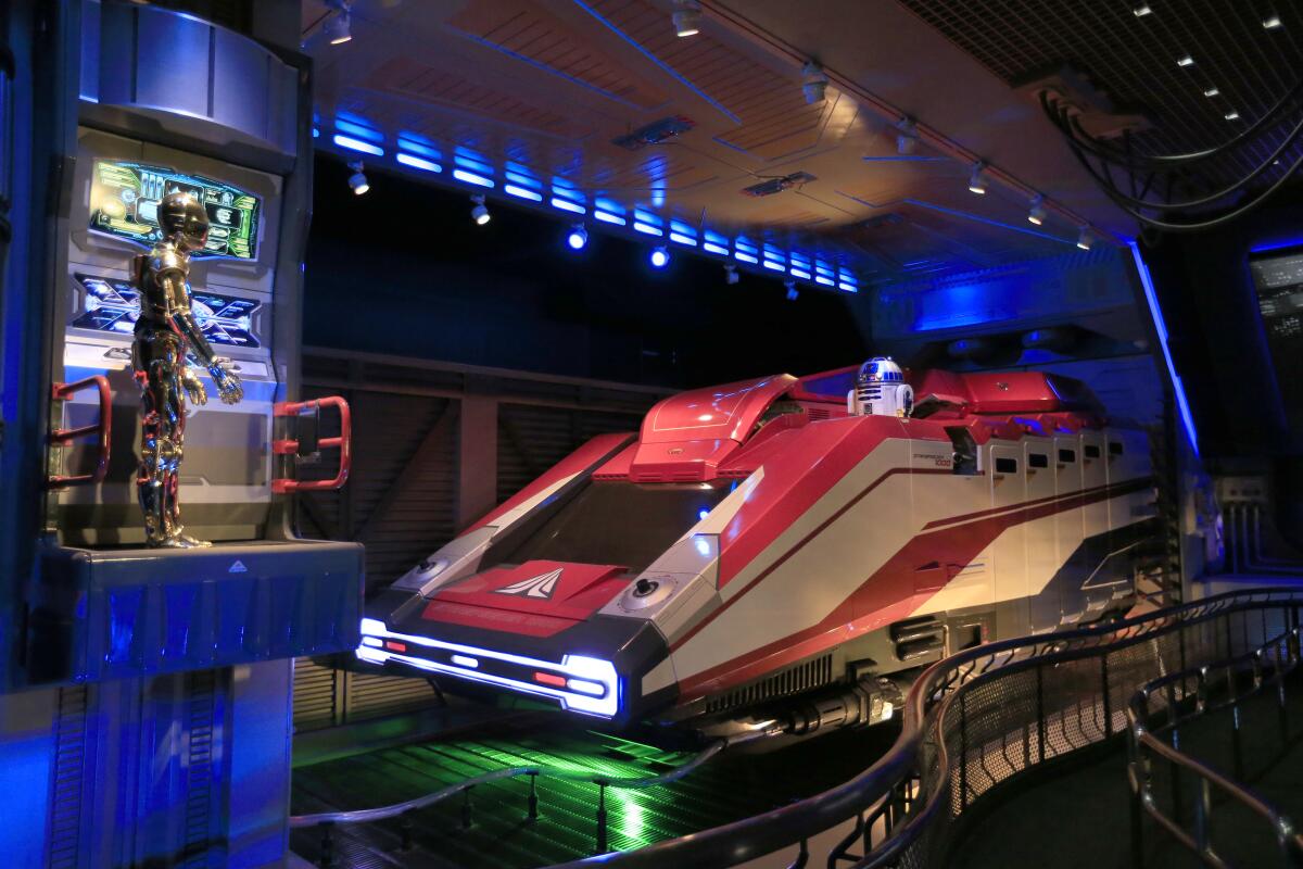 A view of the Star Tours entrance at Disneyland shows a gold robot and a sleek Space Age vehicle.