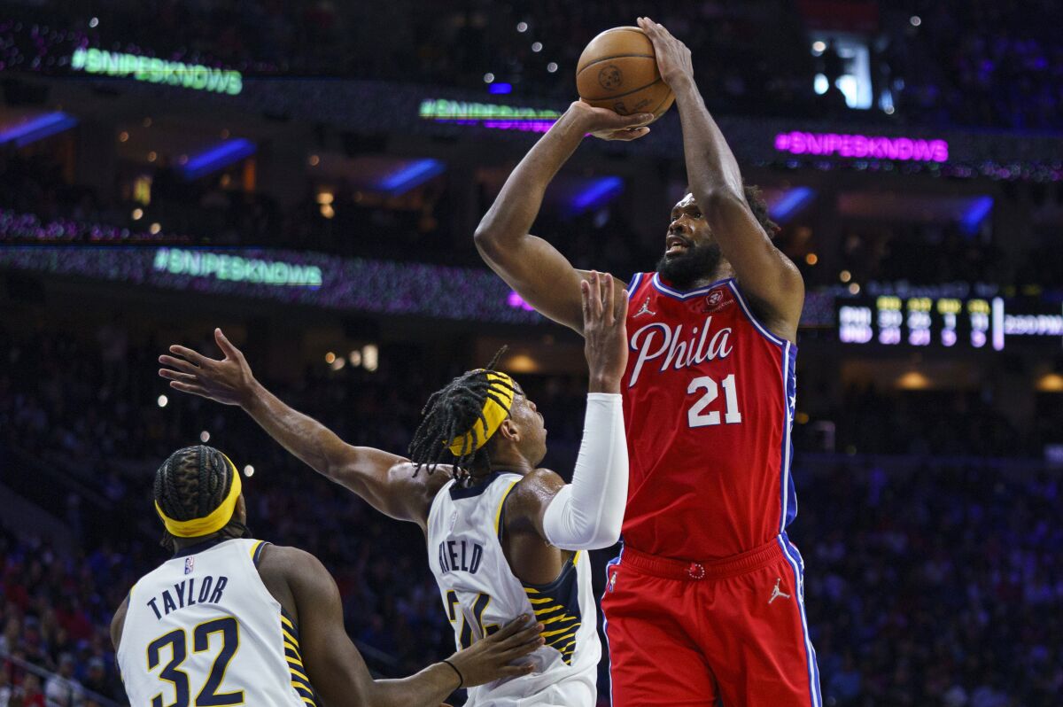 Philadelphia 76ers' Joel Embiid, right, shoots the ball with Indiana Pacers' Buddy Hield, center, and Terry Taylor, left, defending during the second half of an NBA basketball game, Saturday, April 9, 2022, in Philadelphia. The 76ers won 133-120. (AP Photo/Chris Szagola)