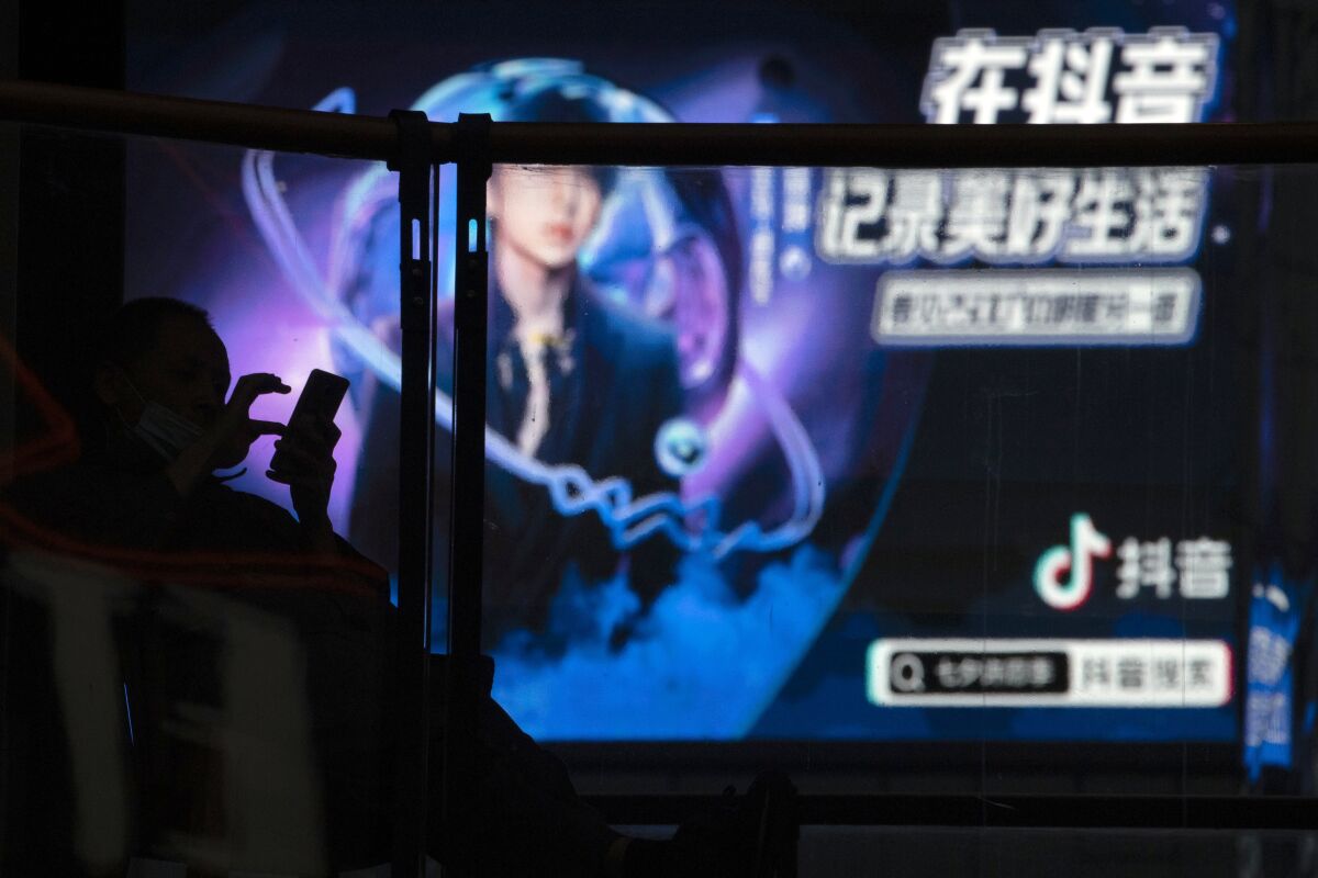 FILE - A man using his smartphone is silhouetted near an advertisement for Douyin, the Chinese sister app of TikTok, at a mall in Beijing on Aug. 30, 2020. A Chinese court in southwestern Sichuan province executed a man Saturday, July 23, 2022, who was convicted of homicide for setting his former wife on fire in September 2020 while she was livestreaming on Douyin, the short video platform, in a case that had drawn national outrage and horror over an extreme case of domestic violence. (AP Photo/Ng Han Guan, File)