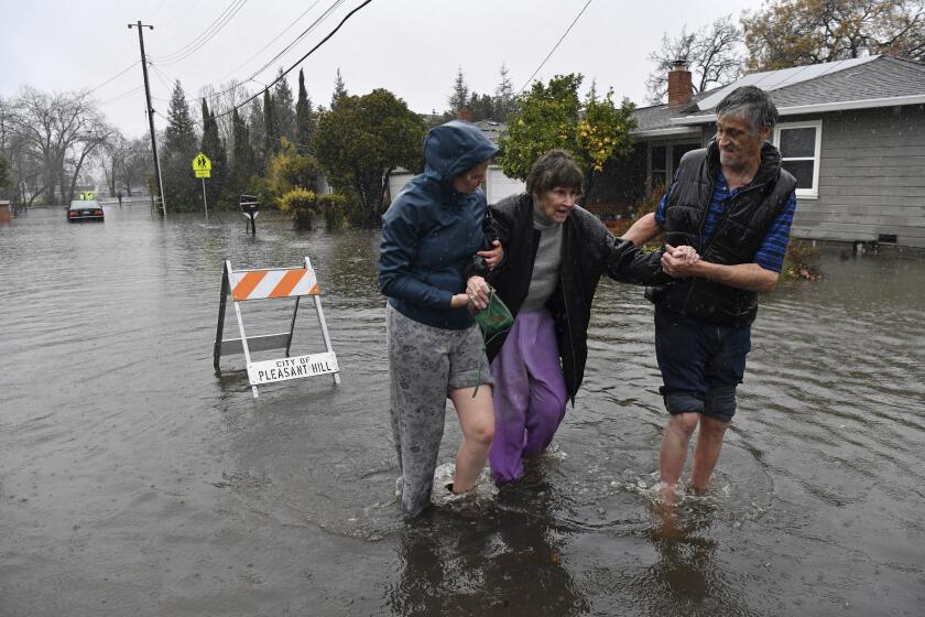 Nurse Katie Leonard, left, assists Scott Mathers, right, as they rescue Mathers' mother, Patsy Costello, 88, after being trapped in her vehicle for over an hour on Astrid Drive in Pleasant Hill, Calif., on Saturday, Dec. 31, 2022. Costello drove her car on the flooded street thinking she could make it when it stalled in the two feet of water. After two hours the water had receded about a foot making it easier to rescue her. Police were called but stood by and watched after calling in a tow truck to help pull the car out of the water. Nurse Katie Leonard, of Pleasant Hill, lives down the block used her kayak to bring Costello hot tea, blankets, food and a phone to call a friend. (Jose Carlos Fajardo/Bay Area News Group via AP)