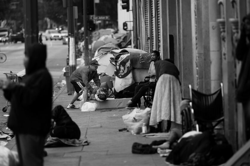 In the morning a man rolls up his bed, on the sidewalk, across the street from The Midnight Mission.