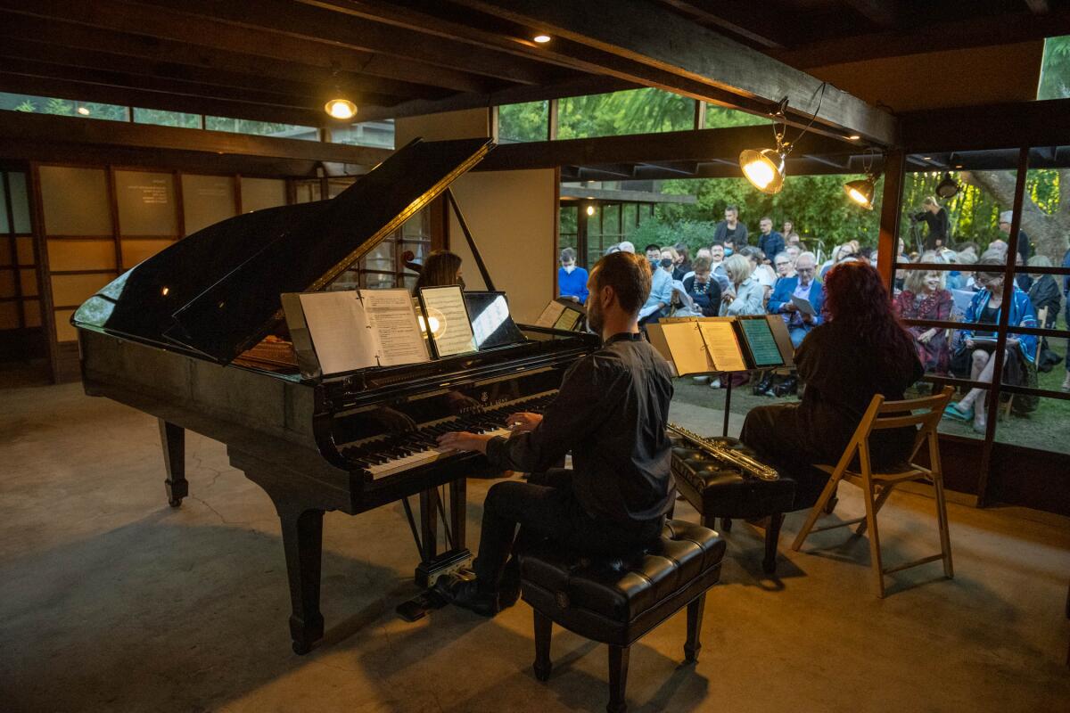 Musicians inside a house play for an audience assembled beyond a set of sliding doors.