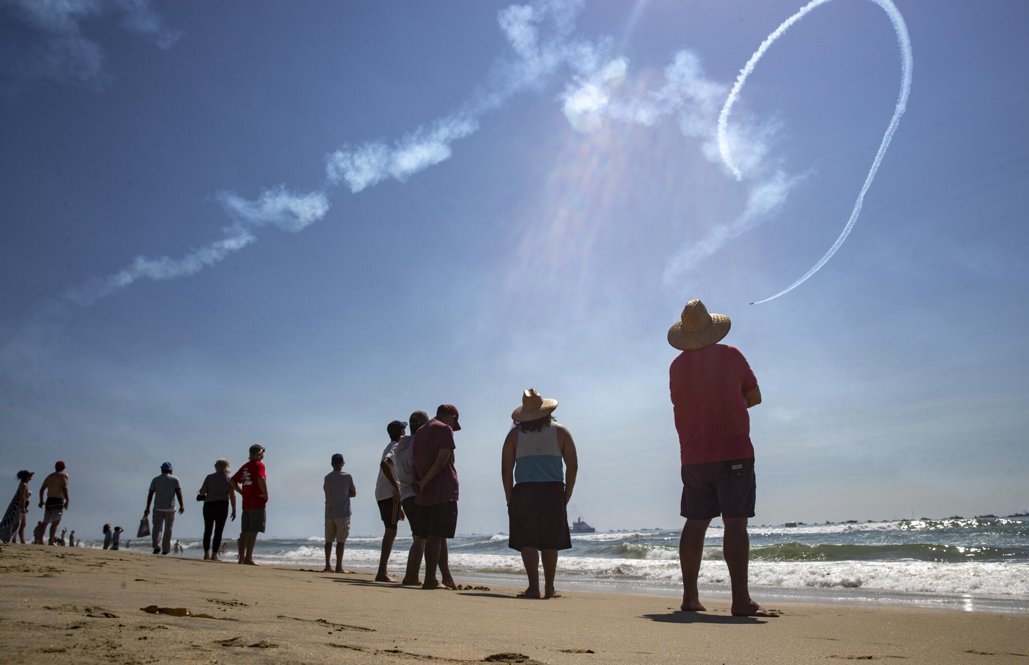 Spectators on the beach watch as a stunt plane pilot performs