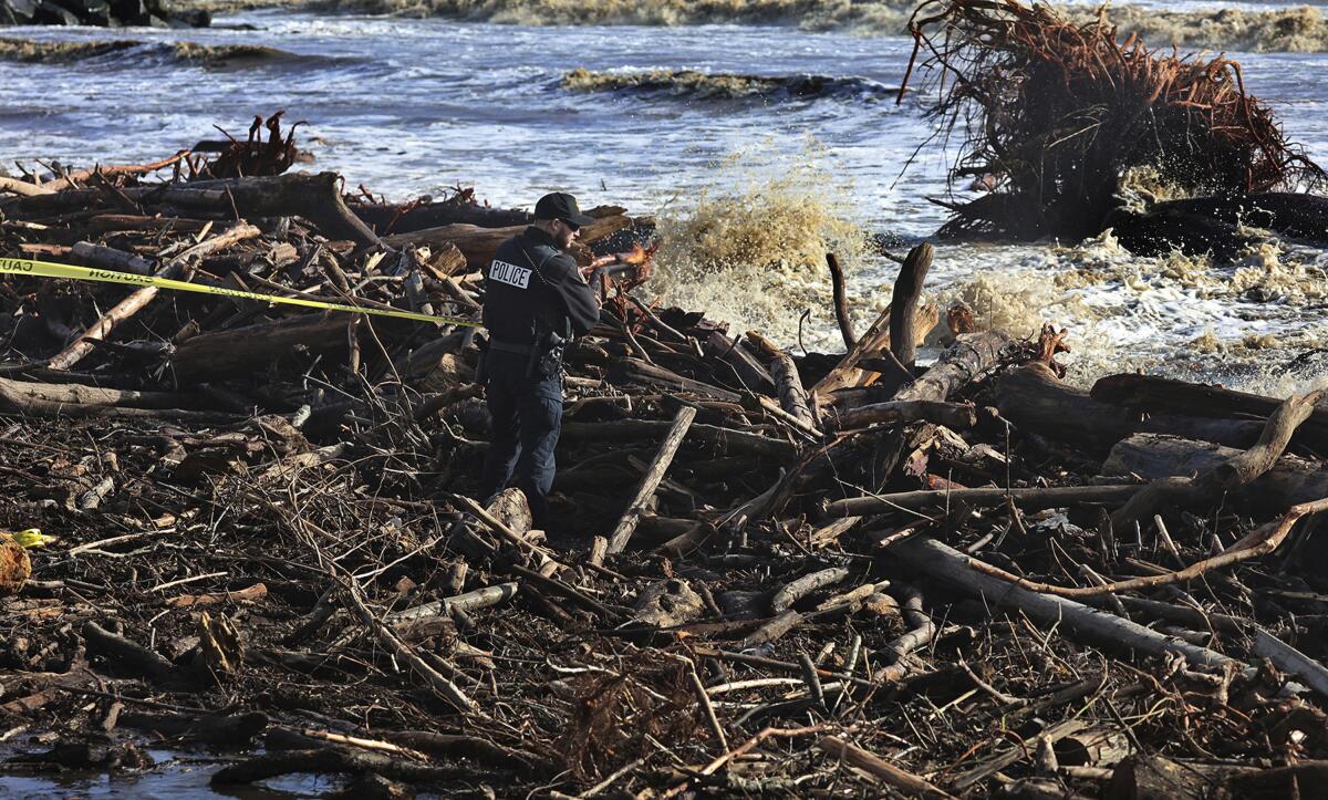 A man stands amid piles of branches and limbs alongside a rushing river.  