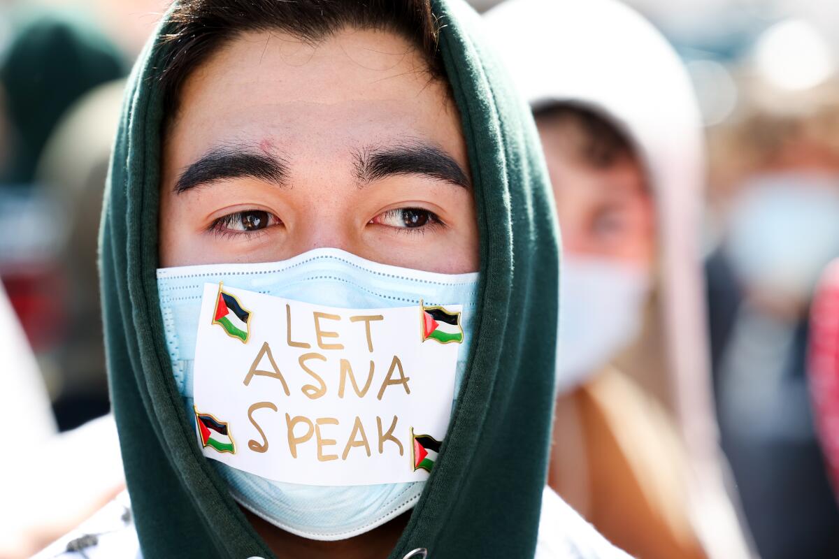 A student wears a face mask with "Let Asna speak" written on it.