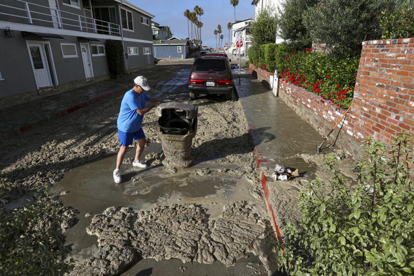 NEWPORT BEACH, CA - JULY 04: Bruce Ogilvie sweeps sidewalk and street in front of his house, flooded by ocean waves that crashed over the sand at the Balboa Pier in Newport Beach and flooded streets. B Street on Saturday, July 4, 2020 in Newport Beach, CA. (Irfan Khan / Los Angeles Times)