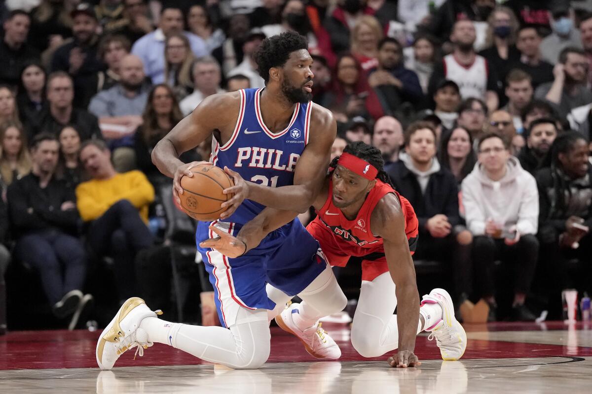 Toronto Raptors forward Precious Achiuwa, right, looks to steal the ball from Philadelphia 76ers center Joel Embiid (21) during the first half of an NBA basketball game Thursday, April 7, 2022, in Toronto. (Frank Gunn/The Canadian Press via AP)