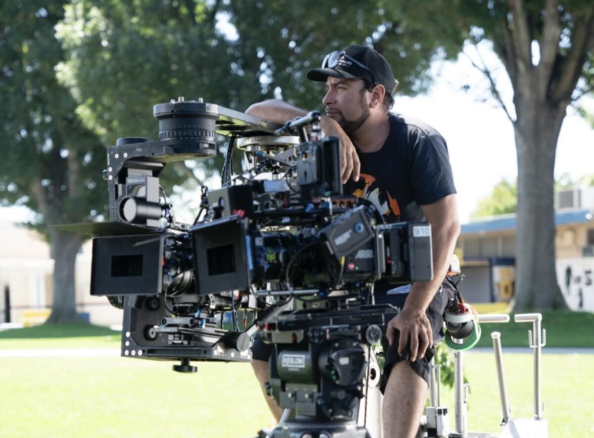 Diego Mariscal, in a black cap and T-shirt, sits on a camera dolly.