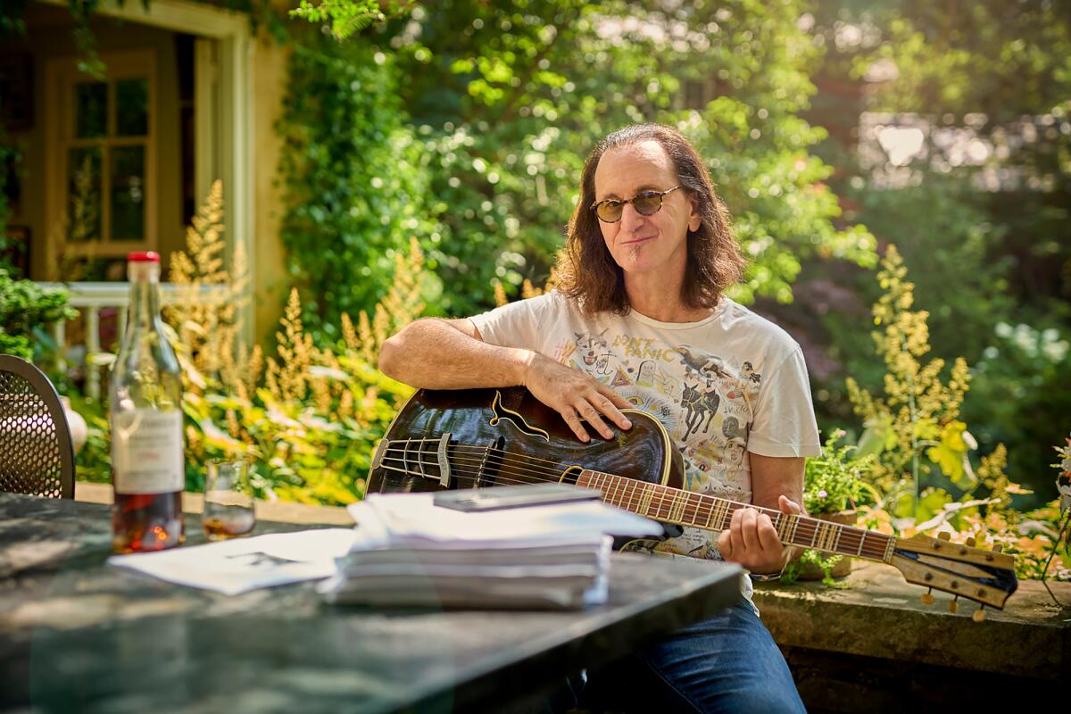 A man with long hair sits outside holding a guitar.