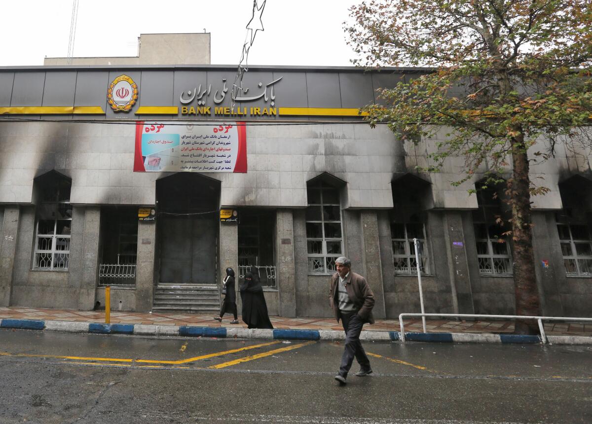 Iranians on Thursday walk past a bank in Shahriar that was damaged during demonstrations against gasoline price hikes.