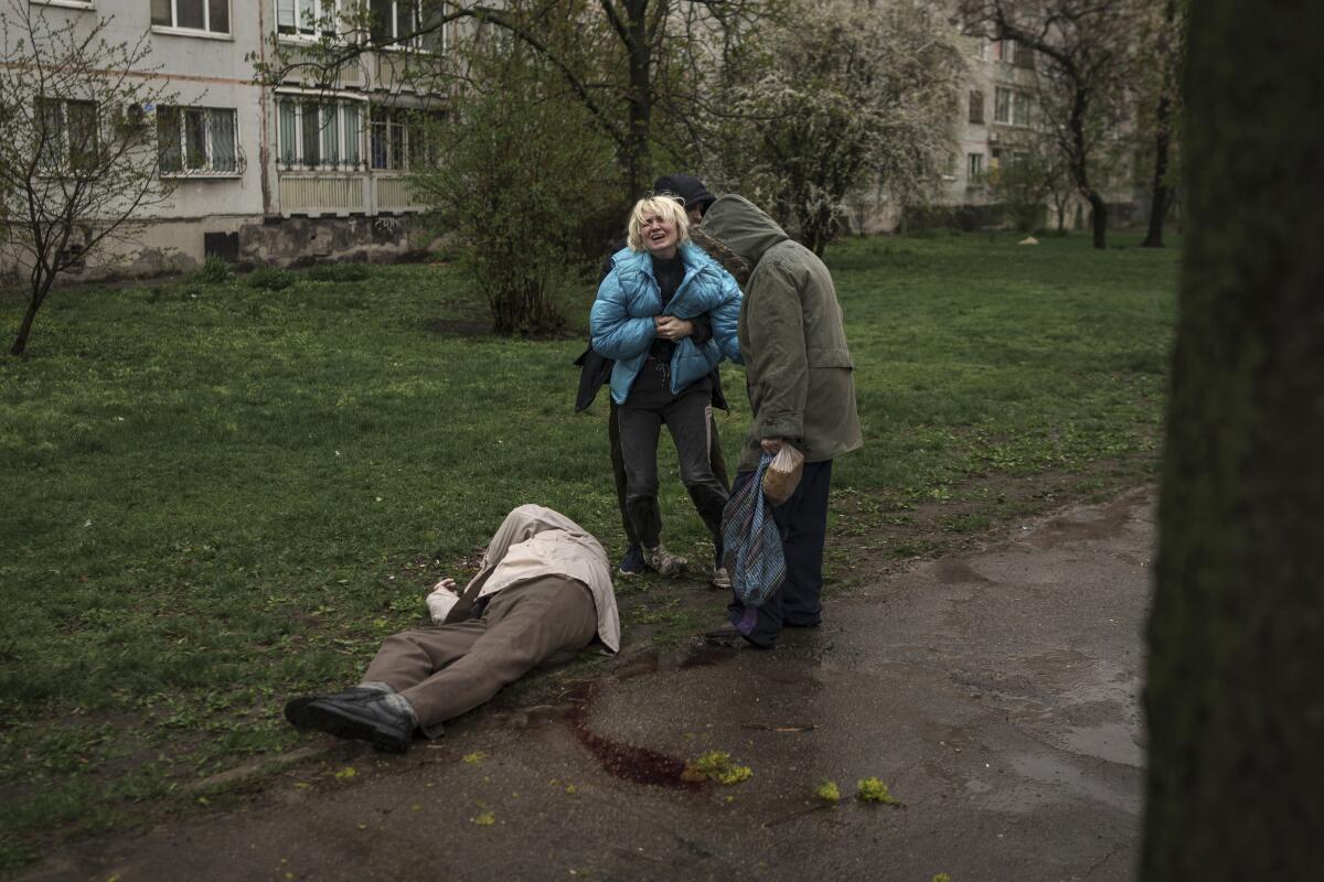 A woman cries next to the body of her father, lying on the ground