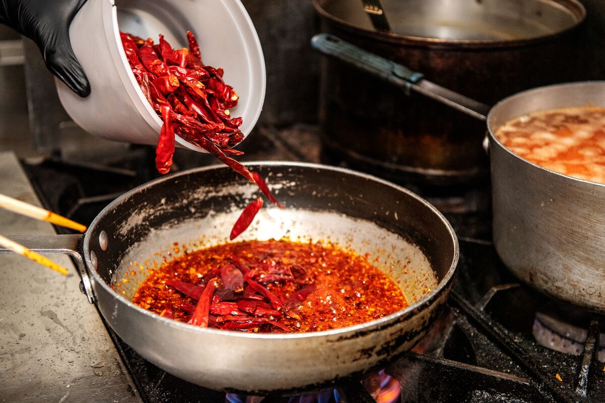 Pouring chiles into a pot on a stove.
