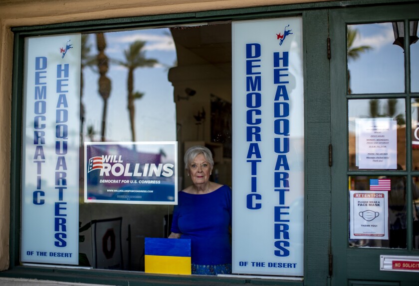 A woman looks out from a window, flanked by signs that say, 'Democratic Headquarters of the Desert'