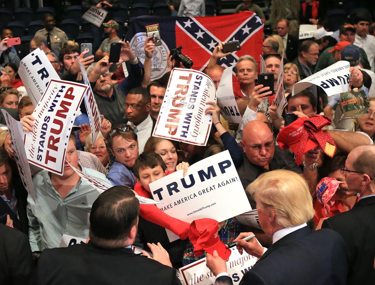 El aspirante a la candidatura presidencial republicana Donald Trump convive con una multitud al término de su segunda visita de campaña a Georgia en el Coliseo Macon Centreplex mientras alguien al fondo sostiene la otrora bandera del estado en Macon, Georgia (Vía AP Foto/Curtis Compton/Atlanta Journal-Constitution)