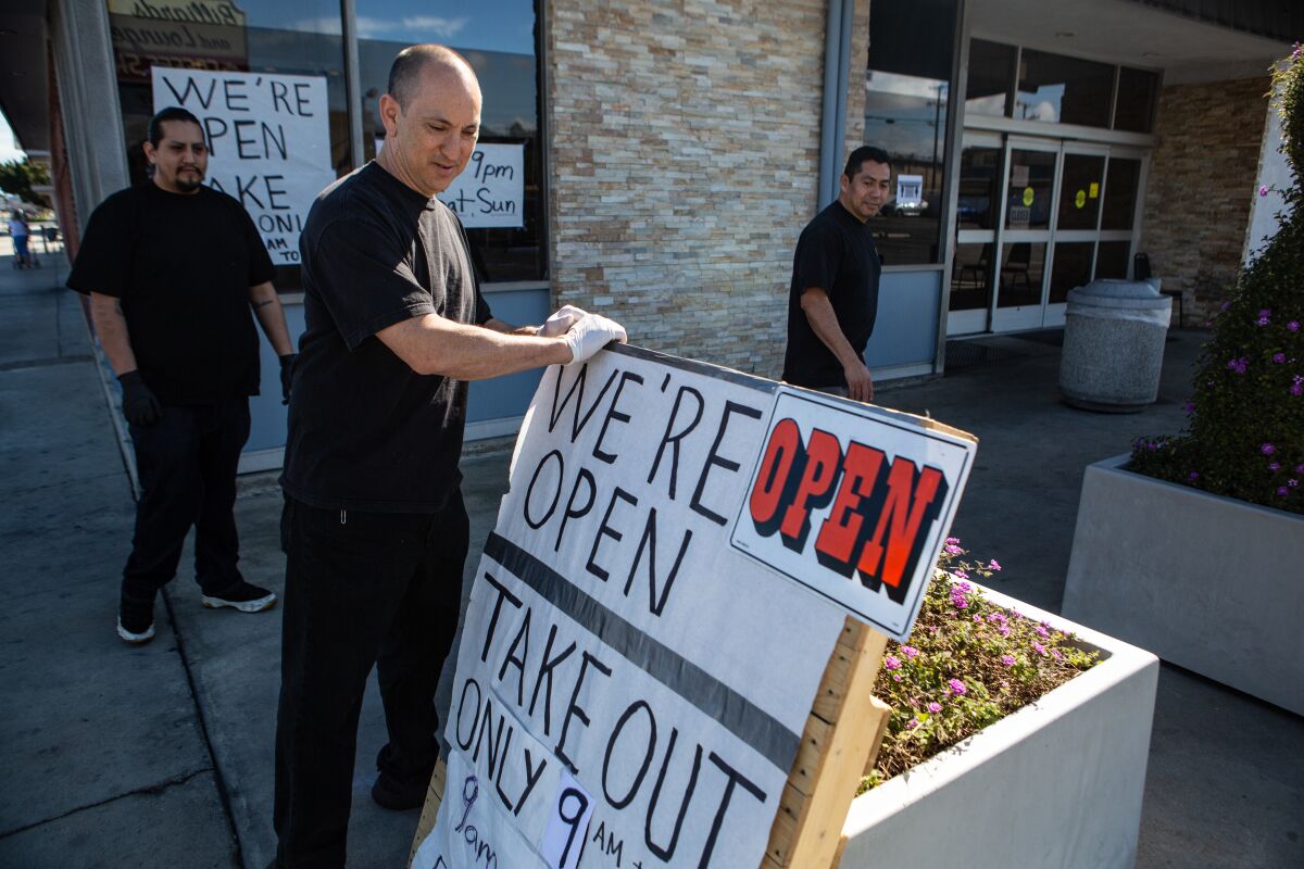 Gardena Bowl Coffee Shop co-owner Frank Nakano positions a "We're Open" sign with new takeout hours.