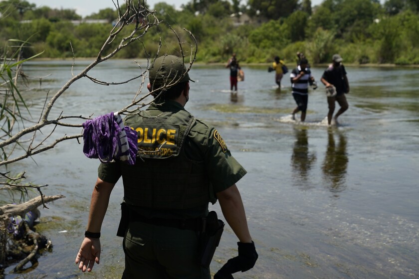 FILE - In this June 15, 2021, file photo, a Border Patrol agent watches as a group of migrants walk across the Rio Grande on their way to turning themselves in upon crossing the U.S.-Mexico border in Del Rio, Texas. A Justice Department attorney says the U.S. Centers for Disease Control and Prevention will issue an order this week about treatment of children under a public health order that has prevented migrants from seeking asylum at U.S. borders. (AP Photo/Eric Gay, File)