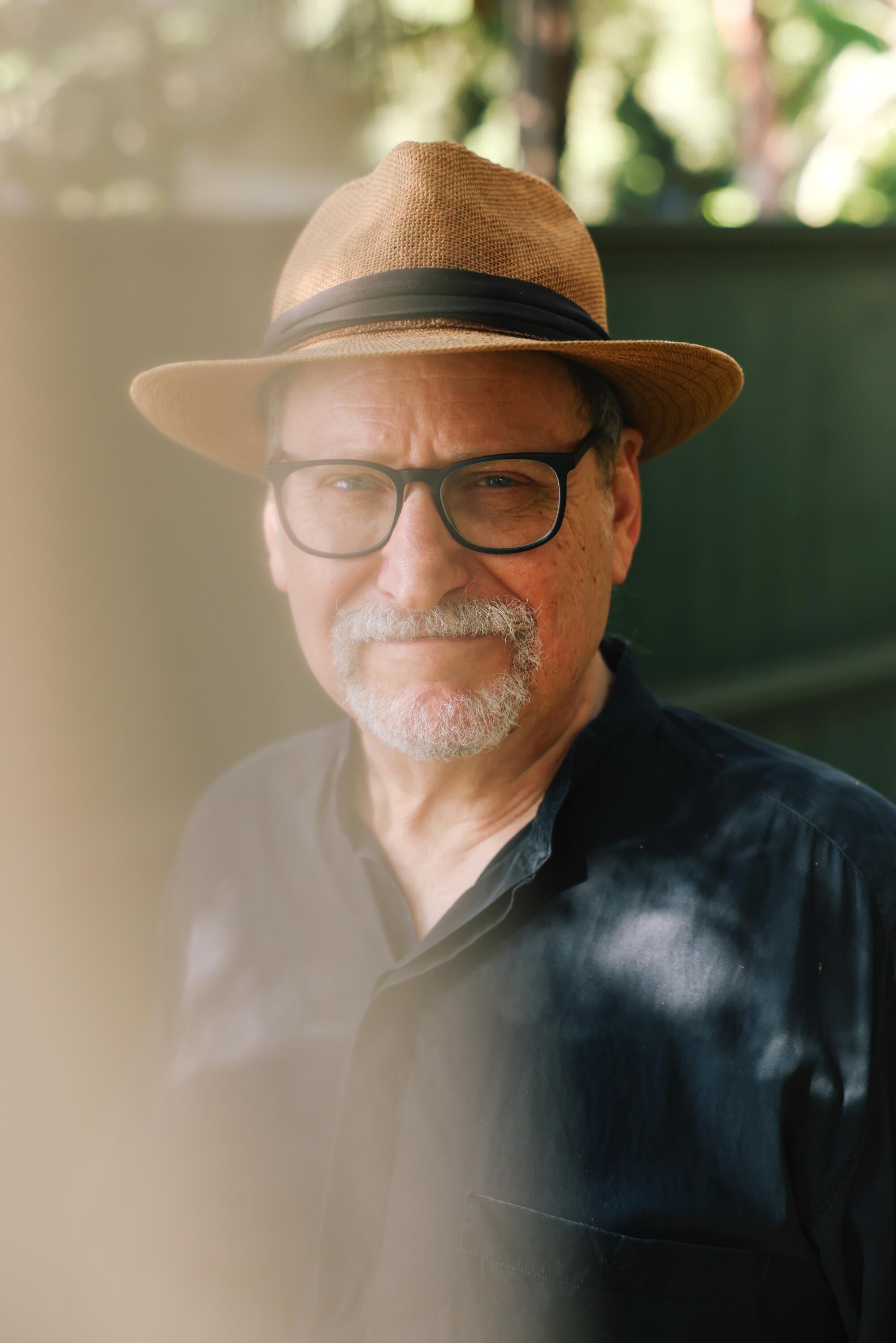 Tom Laichas poses for a portrait in a hat and glasses