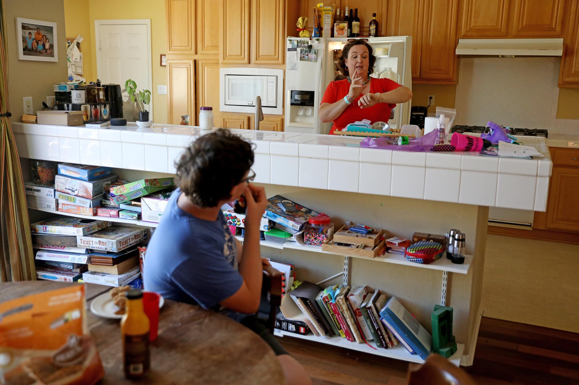 Katie Porter stands in her kitchen, gesturing at her watch as a boy turns toward her in his seat at a table in the next room