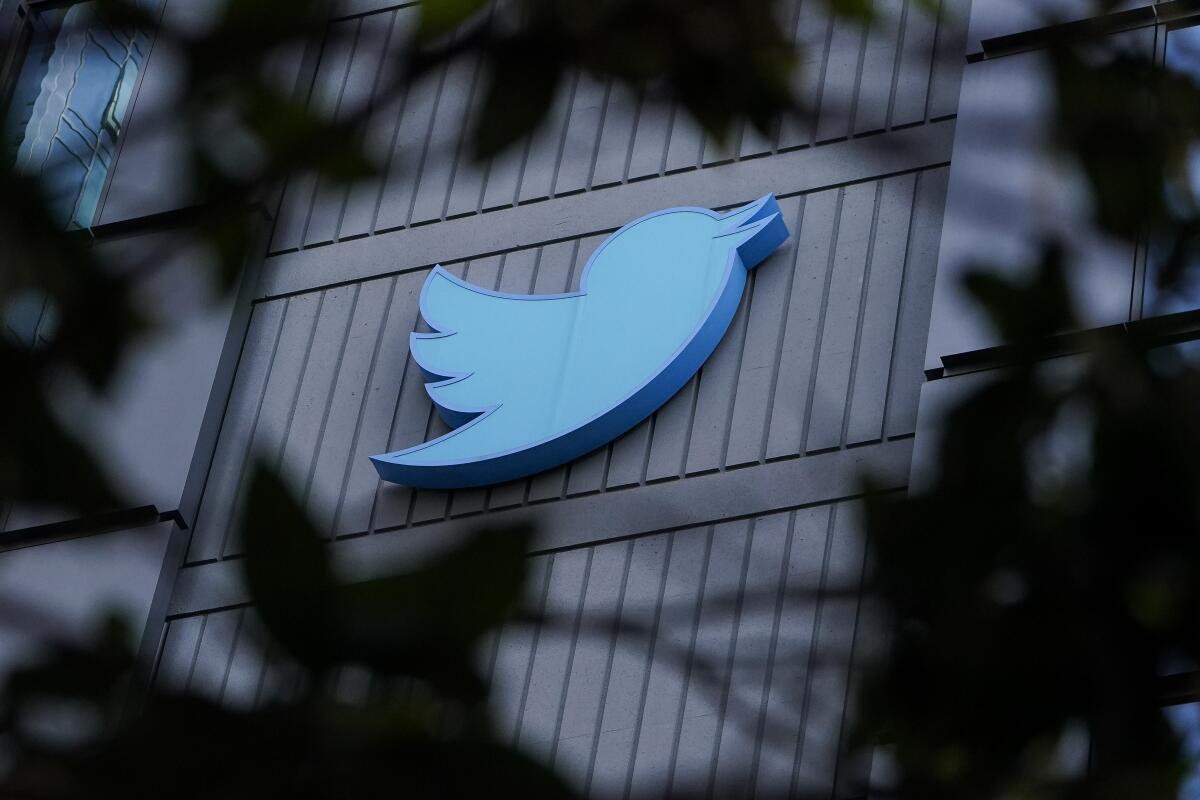 Twitter's blue bird logo on an office building peeks through branches 