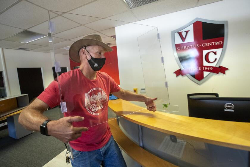 SUN VALLEY, CA - SEPTEMBER 28, 2020: Mike Custer, Director of Facilities at Village Christian School in Sun Valley, installs a temporary sneeze guard made out of plexiglass inside the central office reception room, to protect against the spread of the coronavirus. A larger one has been ordered and will arrive soon. The school has made $100,000 worth of investment into in-person schooling. (Mel Melcon / Los Angeles Times)