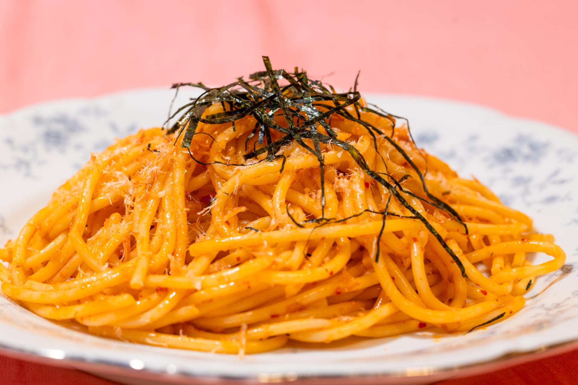 A plate with a pile of orange pasta topped with shreds of nori