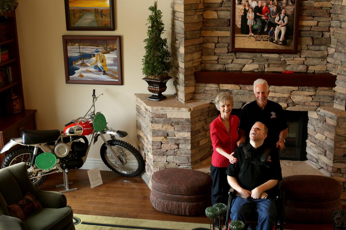 Tom White, with his son Brad and wife Dani in their living room, with one of his prized Husqvarna motocross bikes. (Rick Loomis / Los Angeles Times)