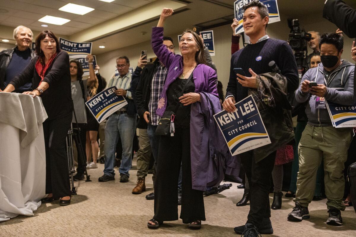 A group of people holding "Kent Lee for City Council" campaign signs cheers in a room
