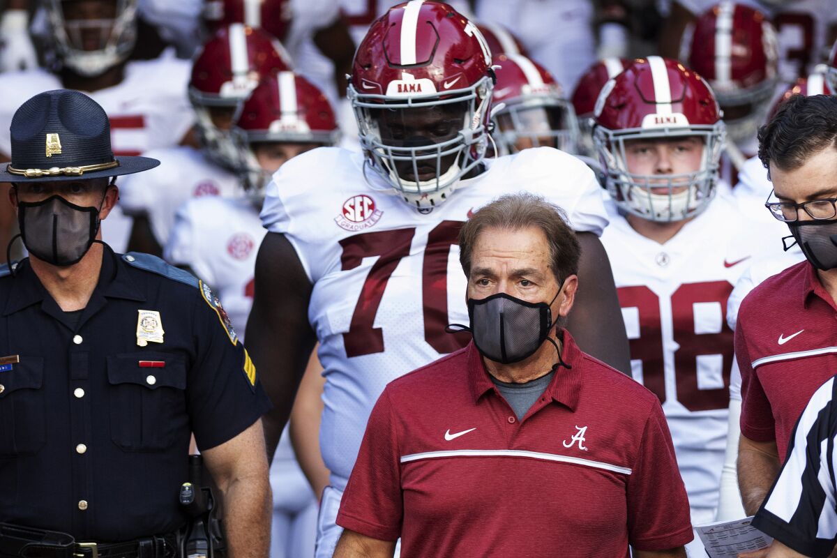 Alabama coach Nick Saban, alongside a law enforcement officer, leads his suited-up team to the field.
