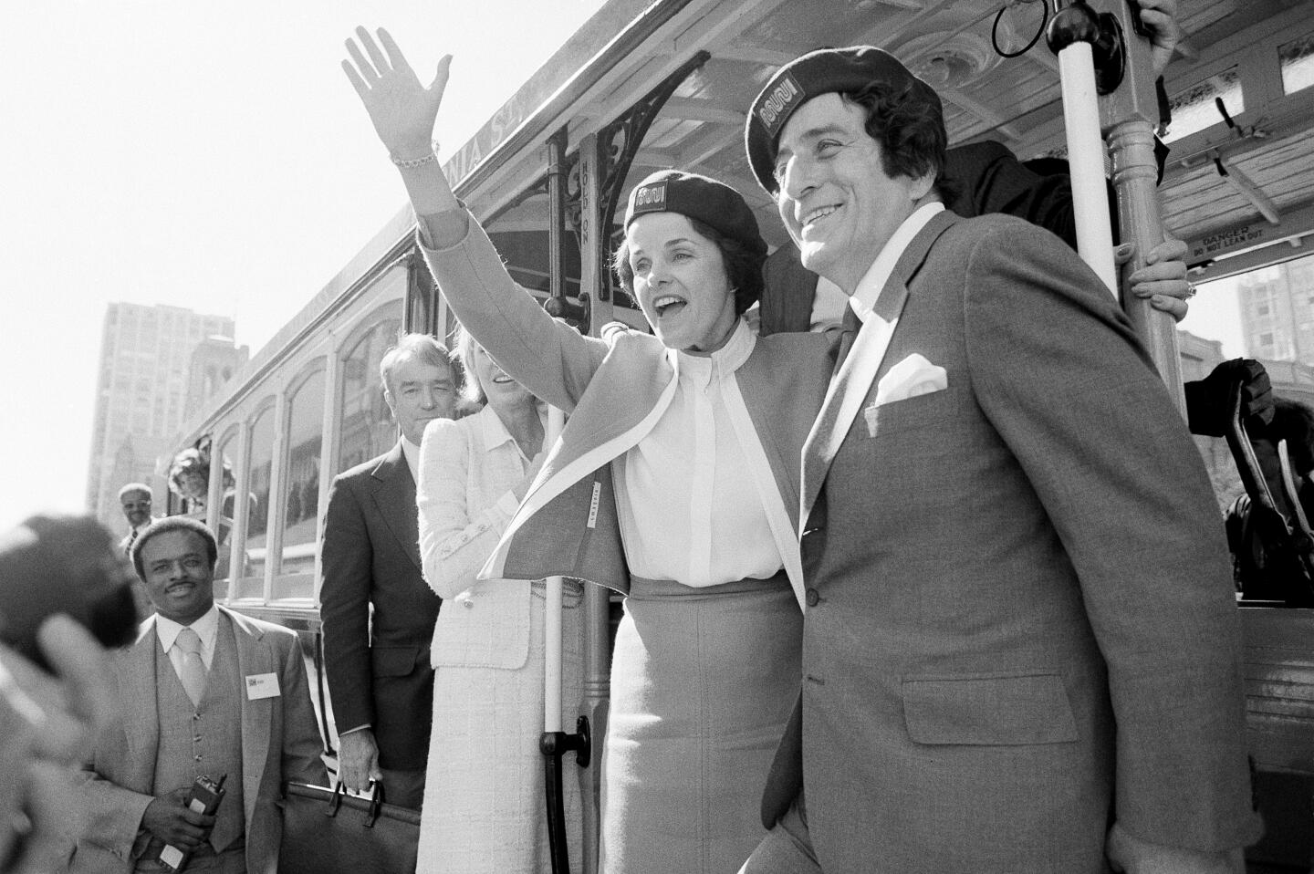an Francisco Mayor Dianne Feinstein and singer Tony Bennett hang on to the outside of a cable car