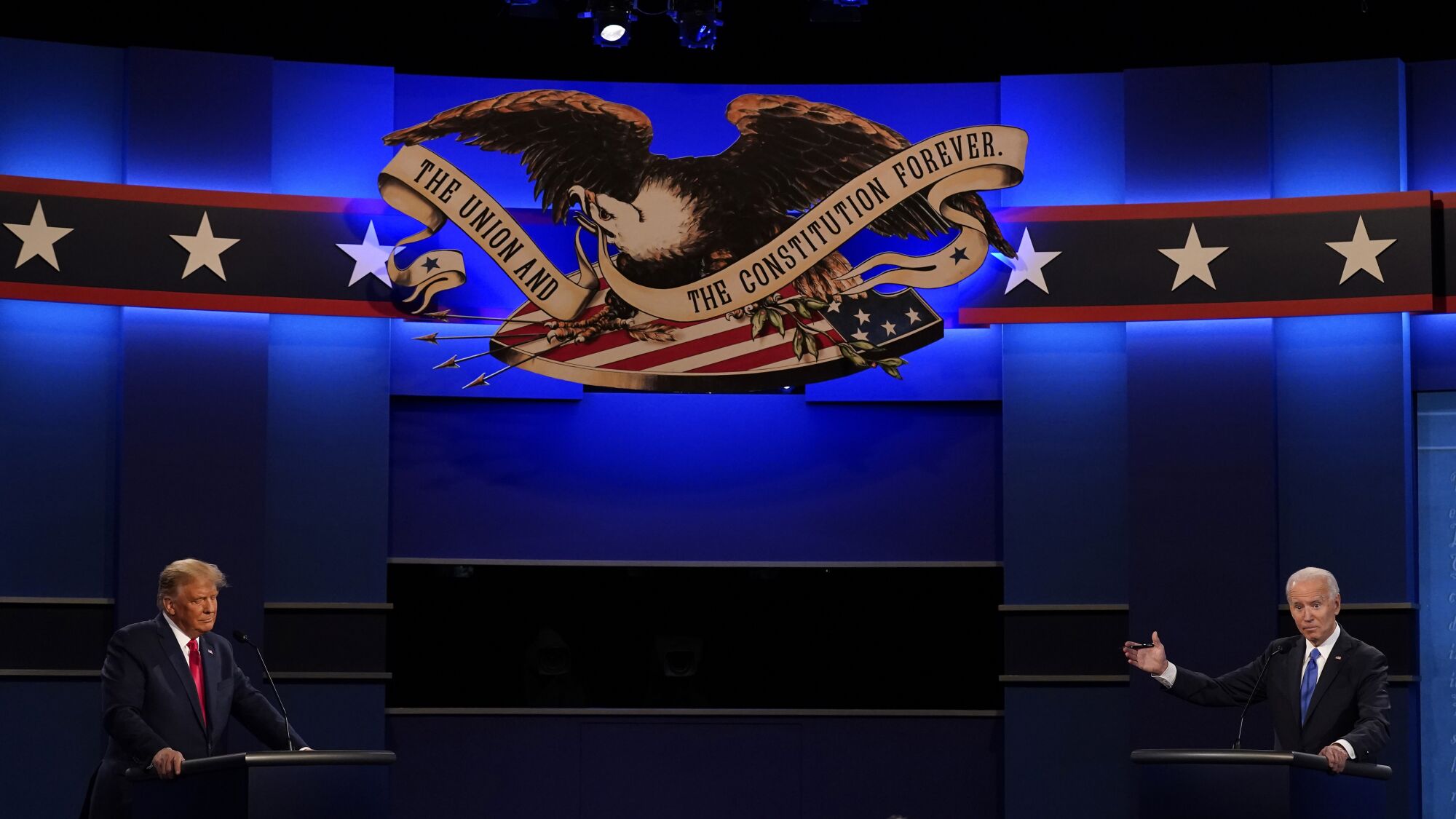 Joe Biden gestures toward President Trump on the debate stage in front of a bald eagle logo