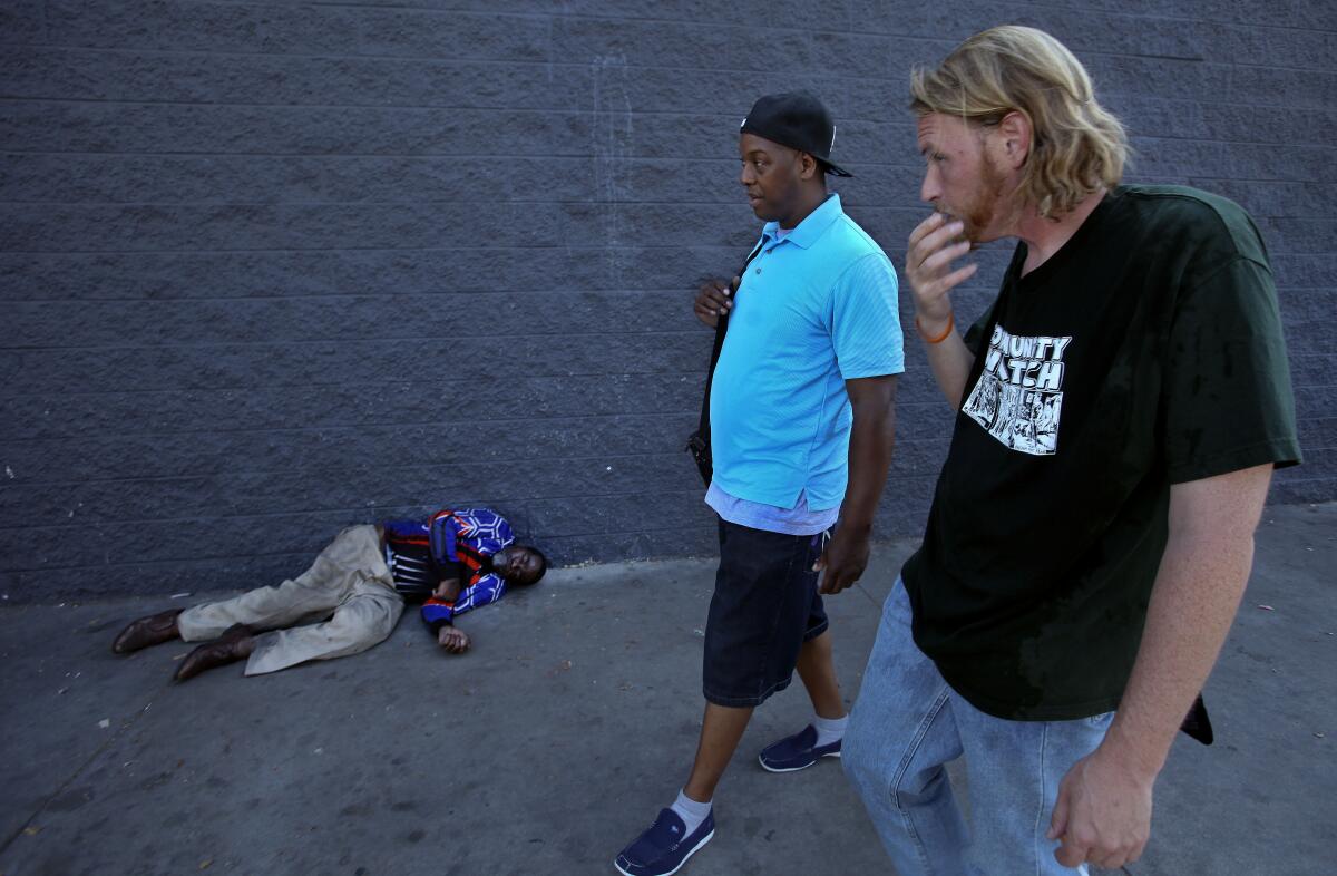 Jeff Page talks with Adam Rice as they walk past a person lying on the sidewalk.