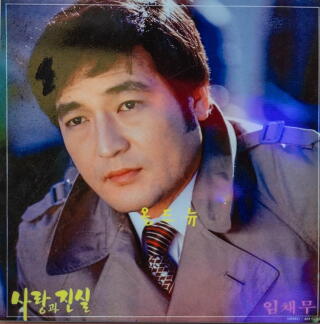 A photo of a man with short dark hair, in a tie and a brown trench coat