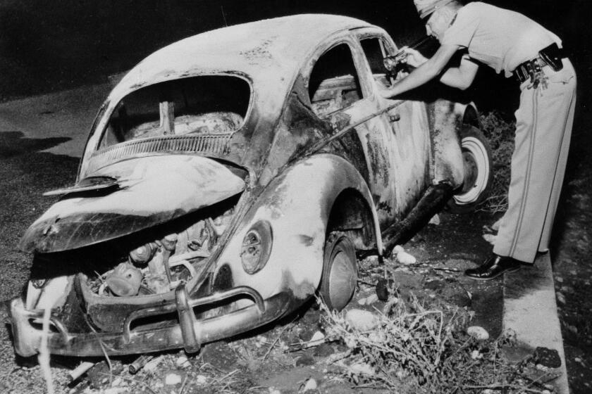 A police officer looks at the seared remains of the Volkswagen Beetle in which dentist Dr. Gordon E. Miller was found dead, in San Bernadino, Calif., Oct. 10, 1964. His wife, Lucille Miller, escaped the fire but has been booked for investigation of murder because of unanswered questions about the origin of the fire and her escape. Police said an empty gasoline can was found in the back seat. (AP Photo)