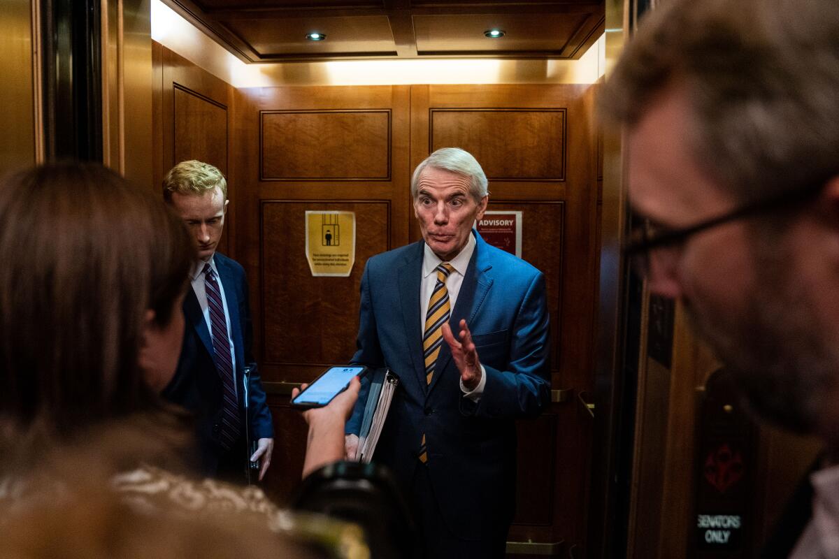 Man in a suit in an elevator talks to reporters