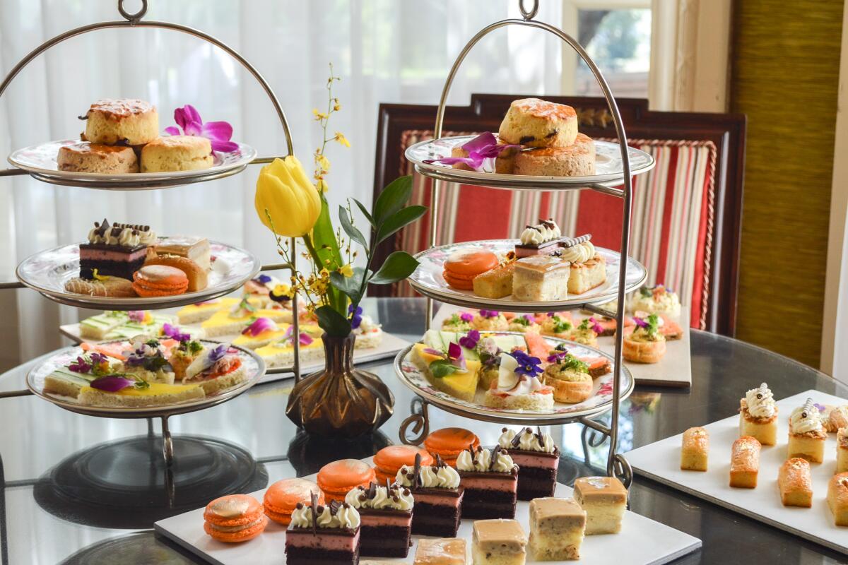 High tea spread with savory sandwiches, sweets and tea in floral china.