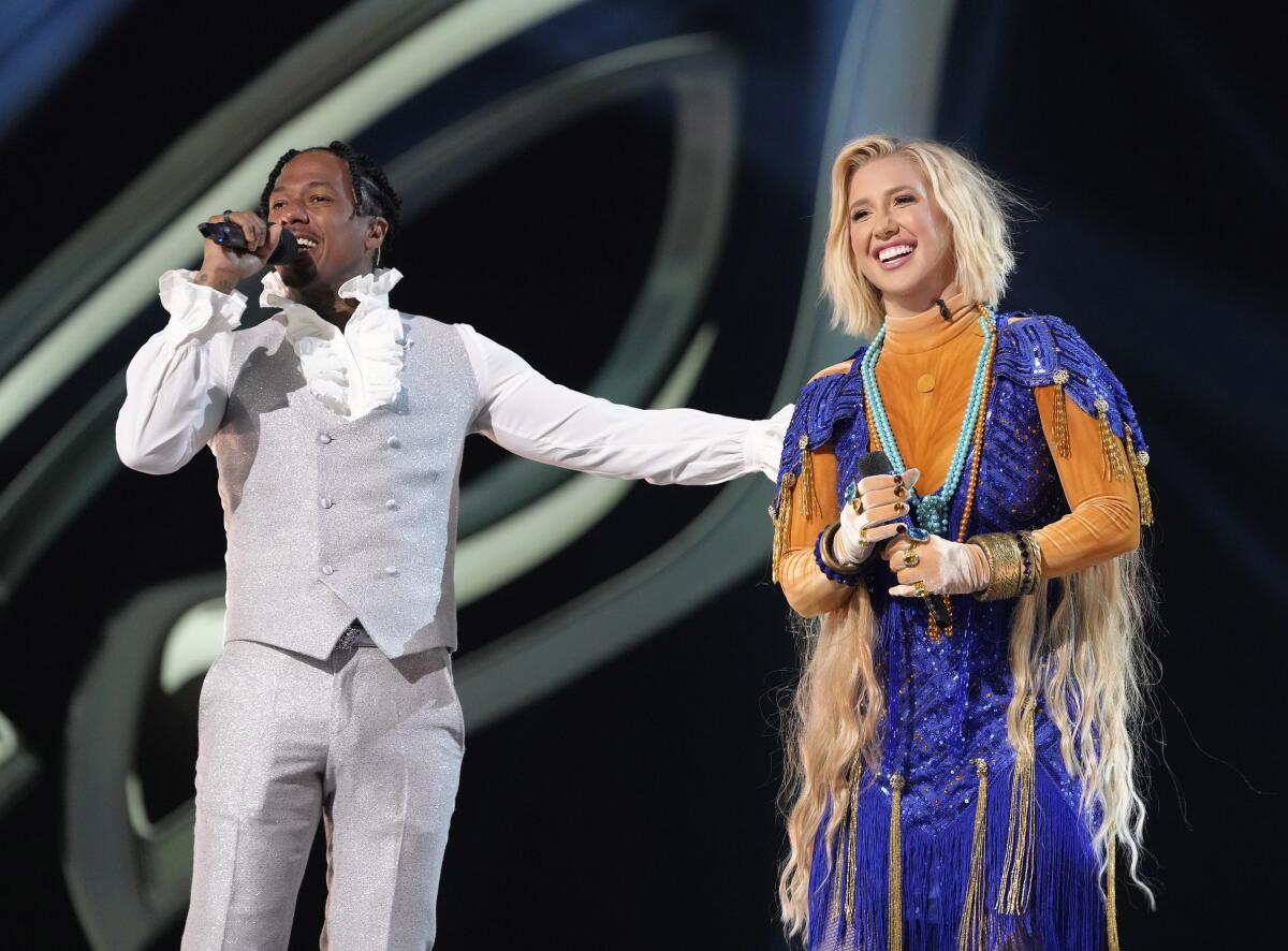 Nick Cannon in a ruffly white shirt and sparkly vest and pants next to Savannah Chrisley in a sparkly, fringed blue dress