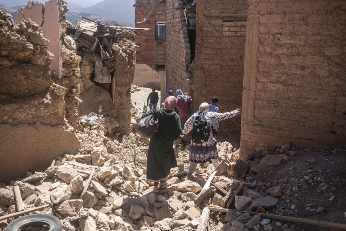 People walk among ruined buildings in Morocco.