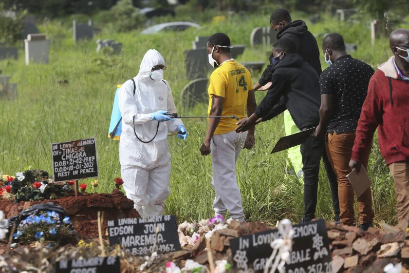 A health worker sprays disinfectant on family members during a burial for a COVID-19 victim in Harare, Zimbabwe.