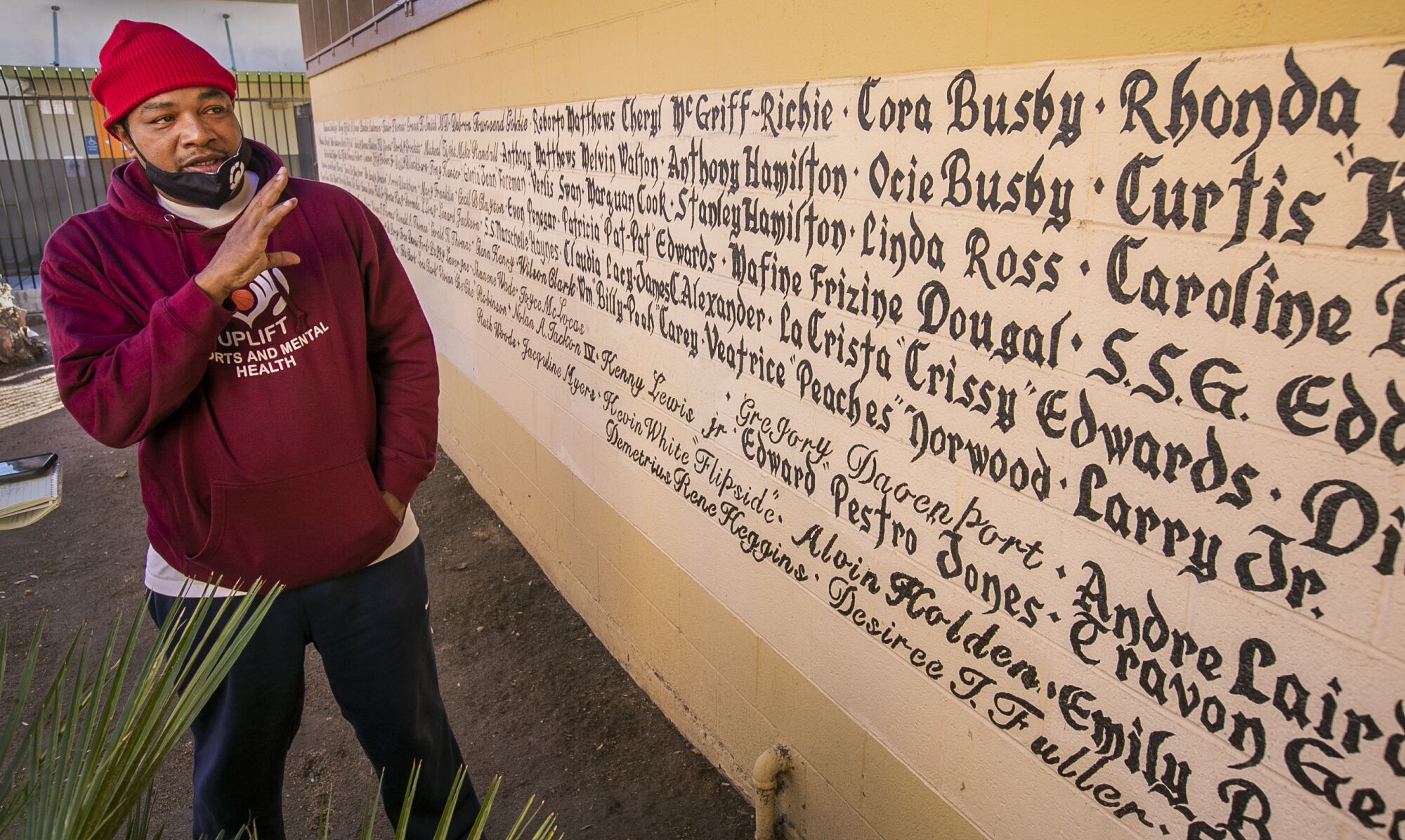 A man stands by a wall of painted names.