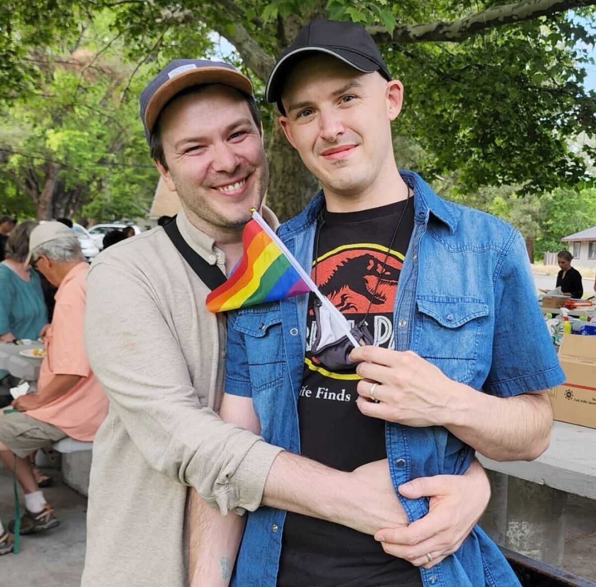 Two men are smiling and holding a mini rainbow flag