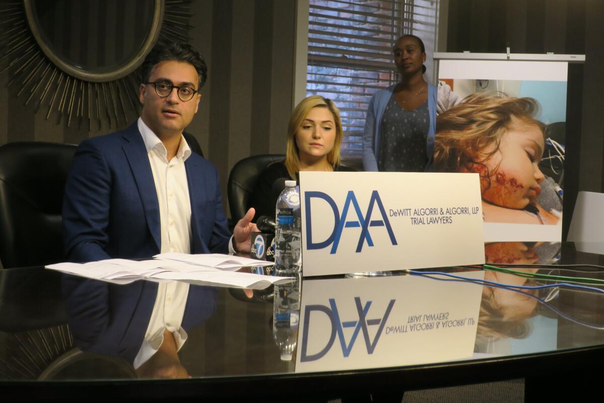 A man and a woman sit at a table near a large photo of a girl with wounds on her cheek.