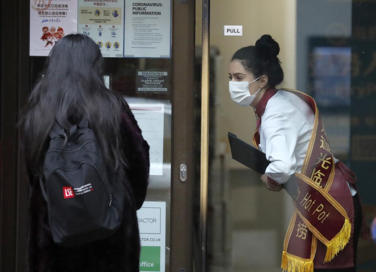 Una empleada de un restaurante de comida china con mascarilla recibe a una clienta en Londres el 5 de marzo del 2020. (AP Photo/Frank Augstein)