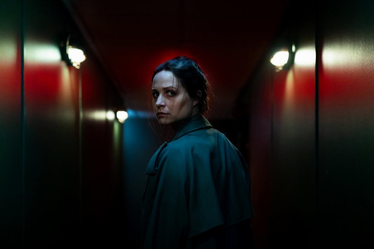 A woman in a dark hallway looks back over her shoulder.